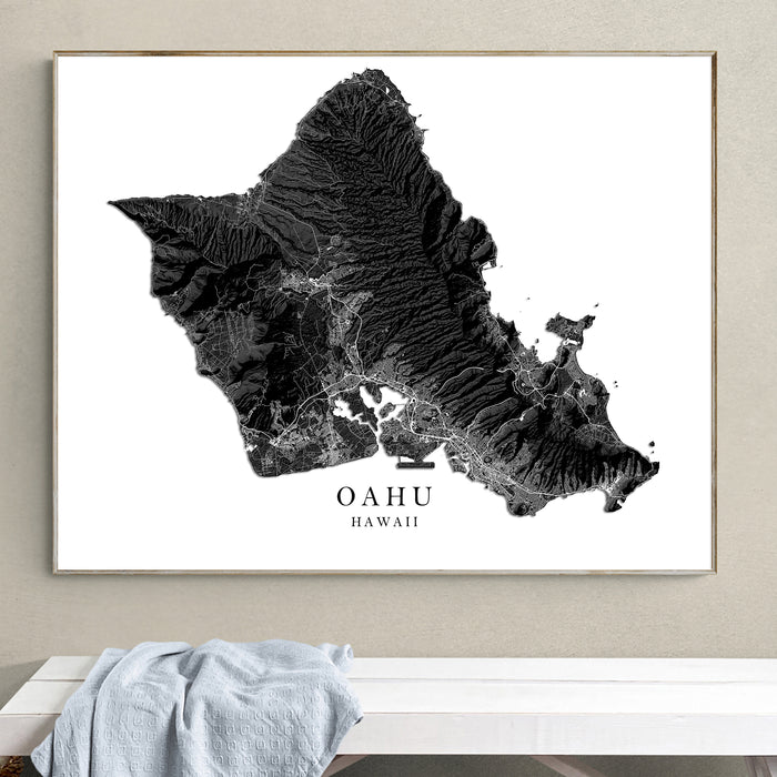 Framed map of Oahu, Hawaii on a wall above a white surface.