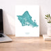 Teal map of Oahu on a white background, displayed on a wooden desk with a laptop and plant.