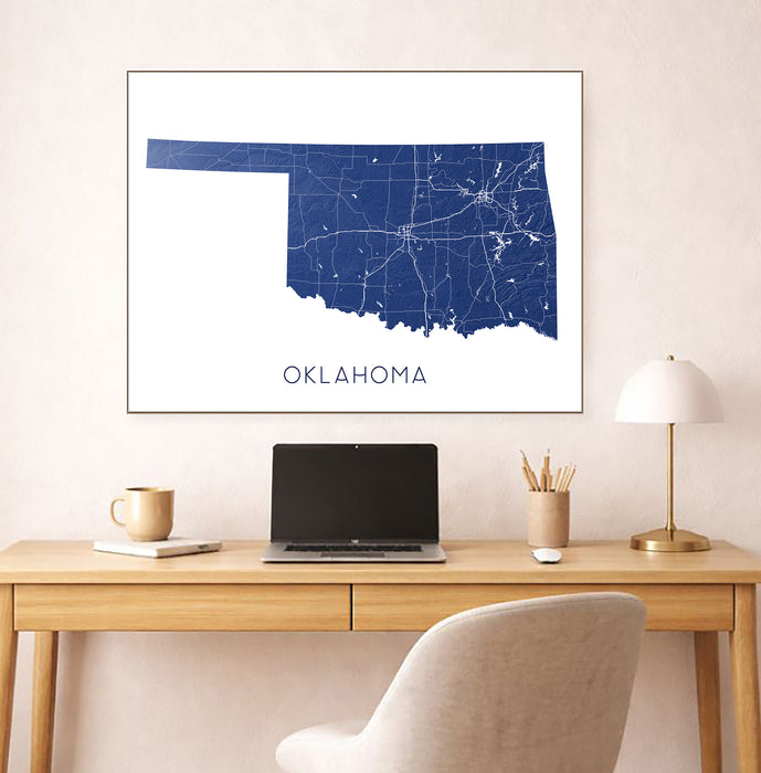 Framed map of Oklahoma on a wall above a desk with a laptop and lamp.