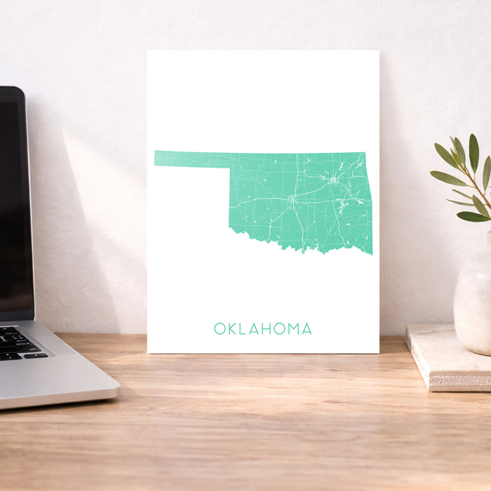 Map of Oklahoma on a white background next to a laptop on a wooden desk.