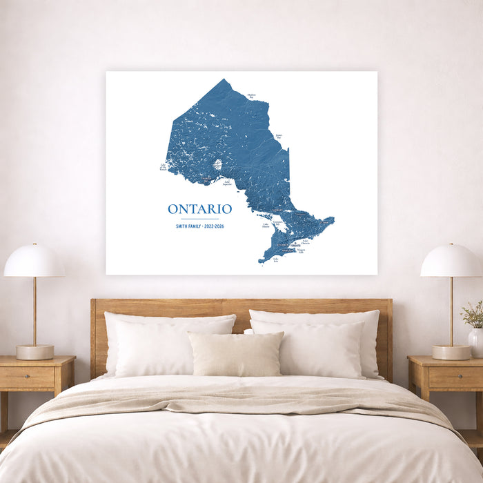 A framed wall art print showing a blue map of Ontario, Canada, displayed above a neatly made bed in a modern bedroom setting with wooden nightstands and lamps.