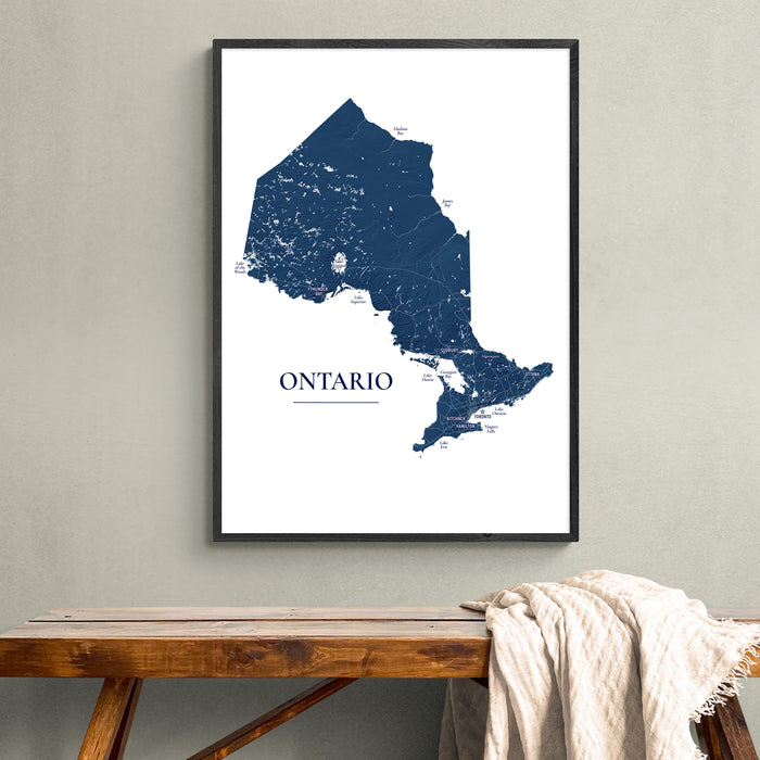 A framed Ontario map print hangs on a light gray wall above a wooden bench with a draped cream throw blanket.
