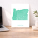 Map of Oregon on a white background next to a laptop on a wooden desk.