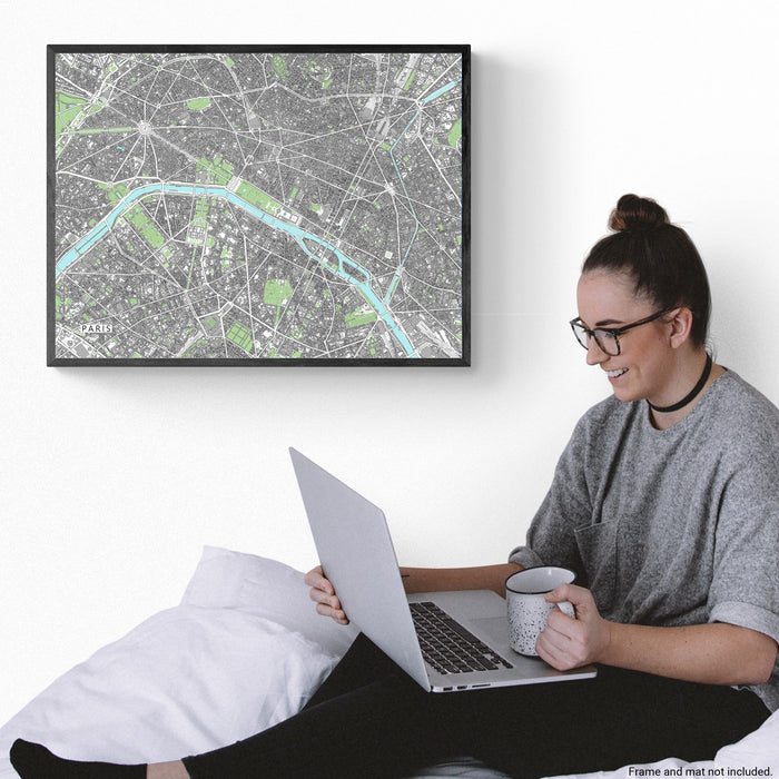 Person sitting on a couch using a laptop with a map of Paris on the wall.