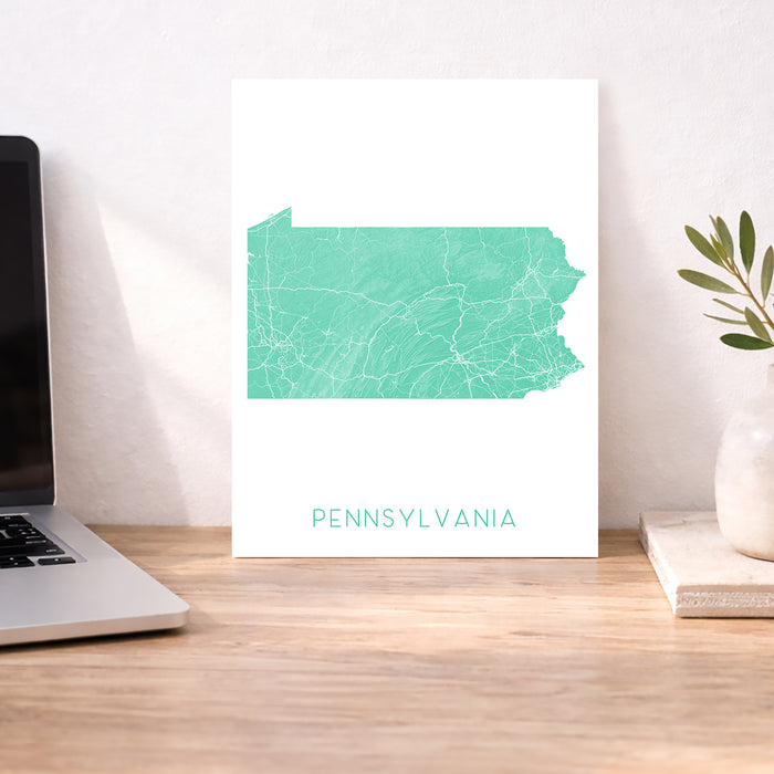 Map of Pennsylvania on a white background next to a laptop on a wooden desk.