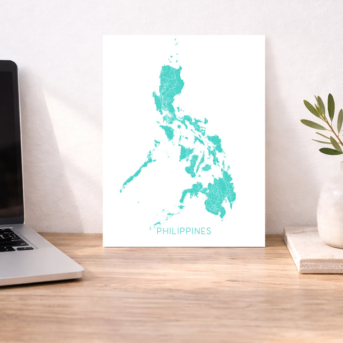 Map of the Philippines on a white background next to a laptop and plant on a wooden desk.