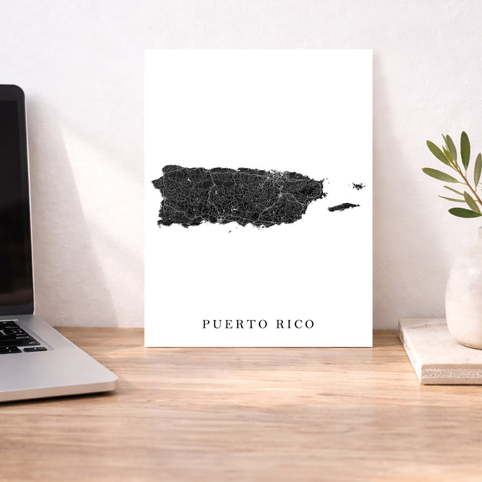 Map of Puerto Rico on a white background next to a laptop on a wooden desk.