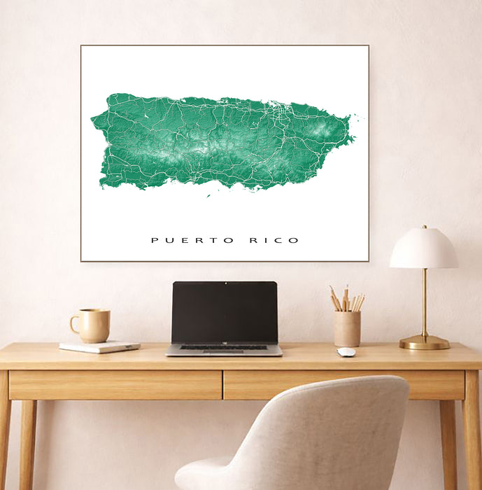 Framed map of Puerto Rico on a wall above a desk with a laptop and lamp.
