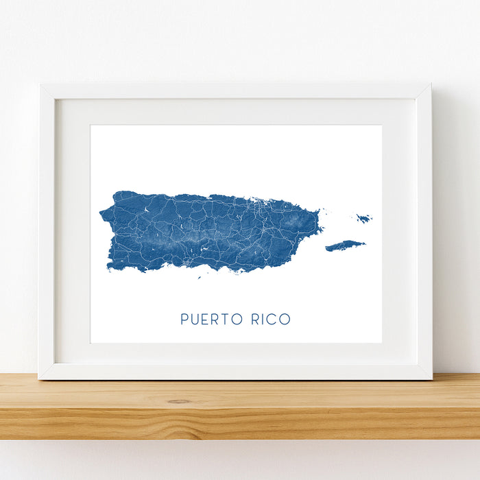 Framed map of Puerto Rico with a white border on a wooden surface.