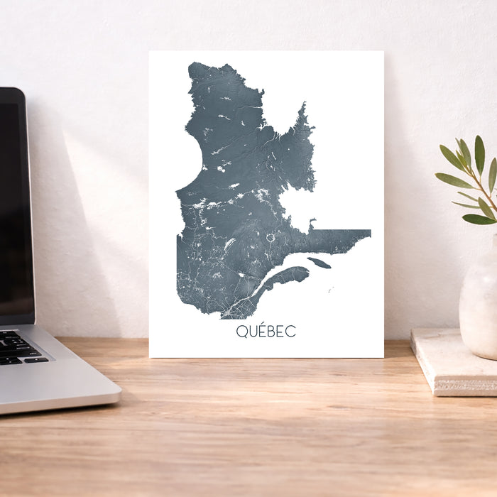 Map of Québec on a white background next to a laptop on a wooden desk.