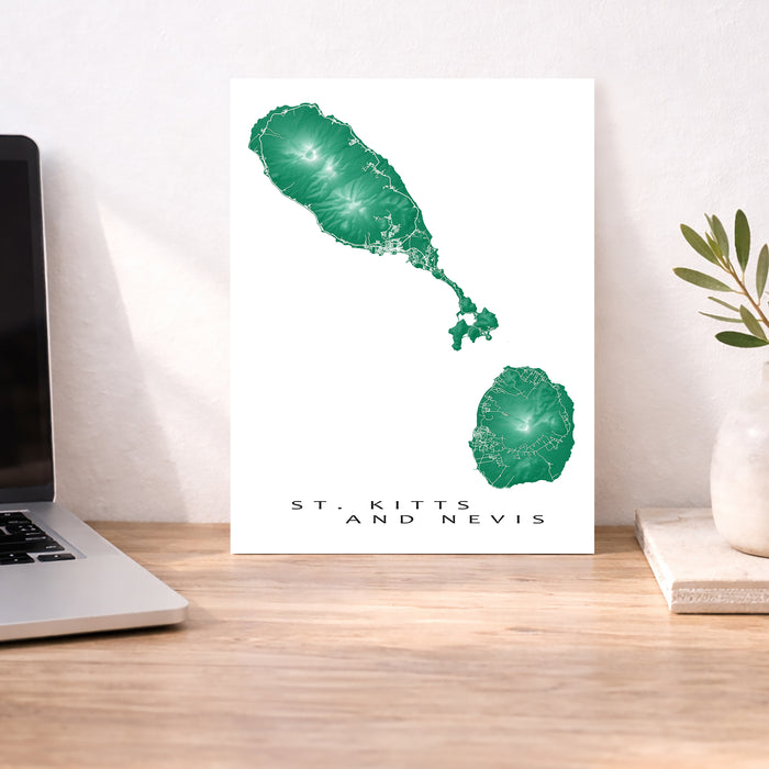 Map of St. Kitts and Nevis on a white background next to a laptop on a wooden desk.