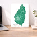 Map of Saint Lucia on a white background next to a laptop and plant on a wooden desk.