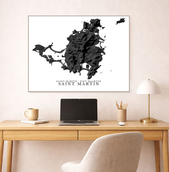 Framed map of Saint Martin on a wall above a desk with a laptop and lamp.