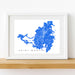 Framed map of Saint Martin with a white border on a wooden shelf.