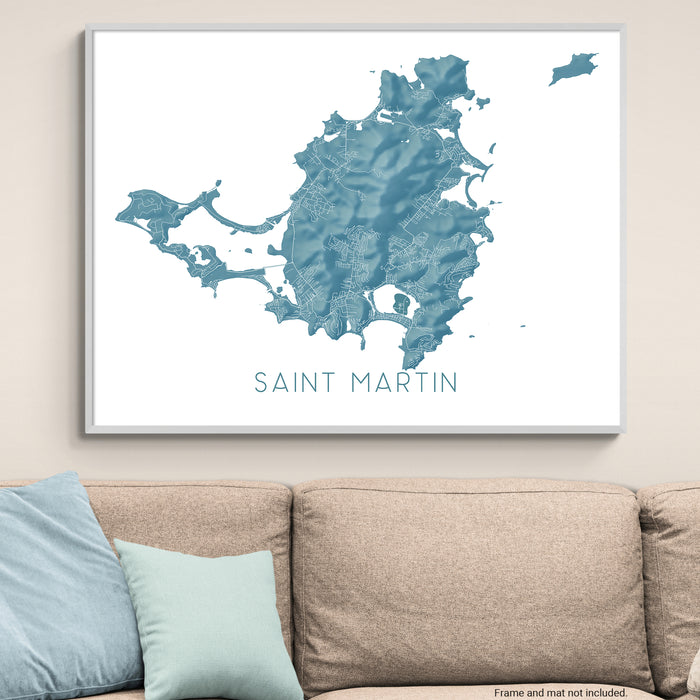 Map of Saint Martin framed on a wall above a beige sofa with light blue pillows.