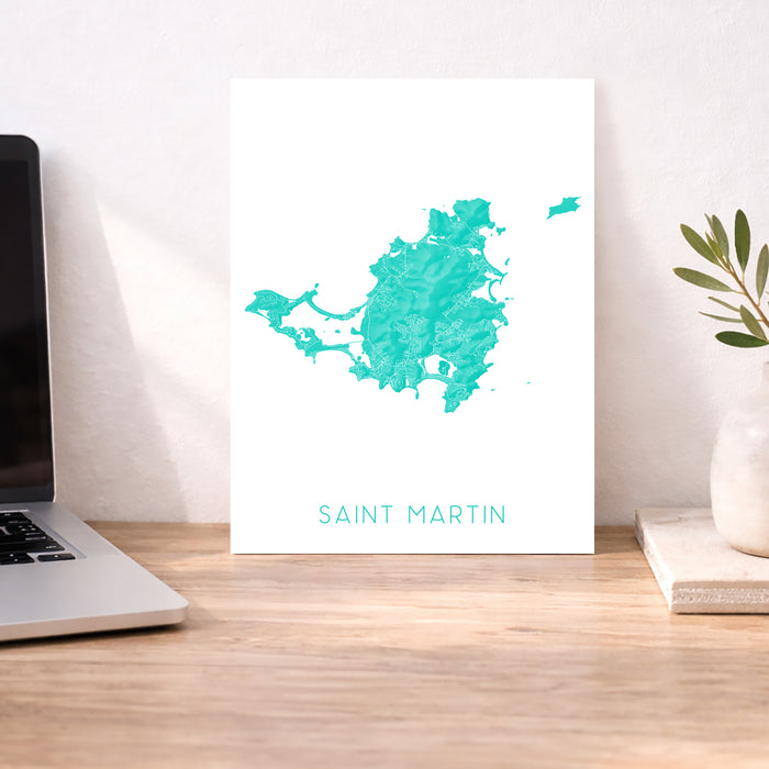 Map of Saint Martin on a white background displayed on a desk with a laptop and plant.