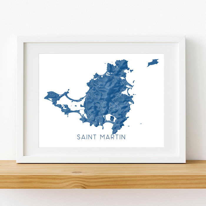 Framed map of Saint Martin on a white wall with a wooden shelf.