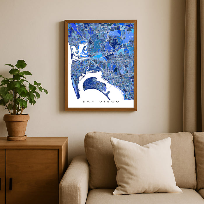 Framed map of San Diego on a wall above a beige sofa with a plant beside it.