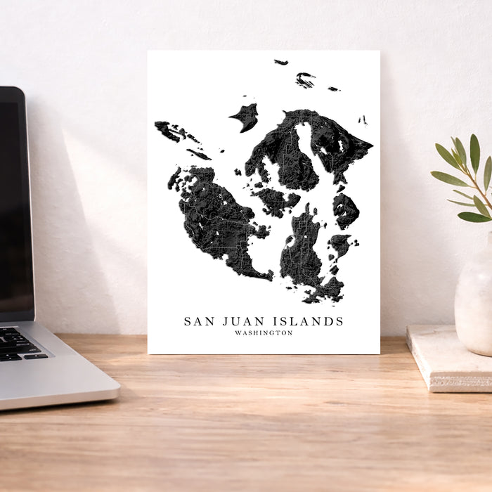 Map of San Juan Islands, Washington on a white background next to a laptop on a wooden desk.
