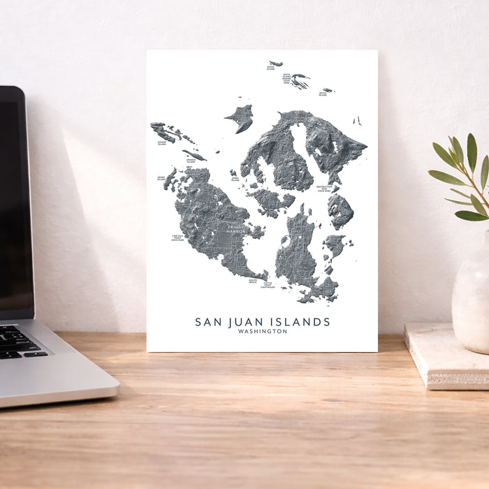 Map of San Juan Islands, Washington on a white background, displayed on a wooden desk with a laptop and plant.