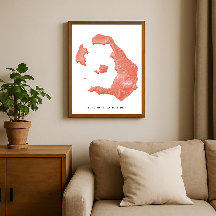 Framed map of Santorini on a wall above a sofa with a plant beside it.