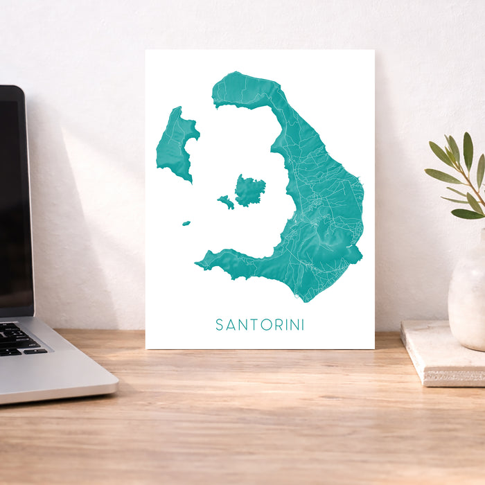 Map of Santorini on a desk with a laptop and plant