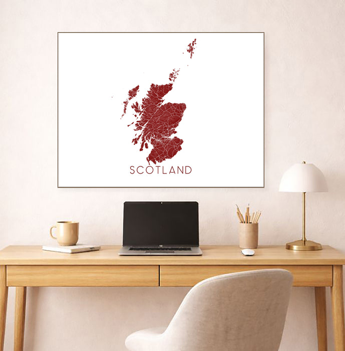 Framed map of Scotland on a wall above a desk with a laptop and lamp.