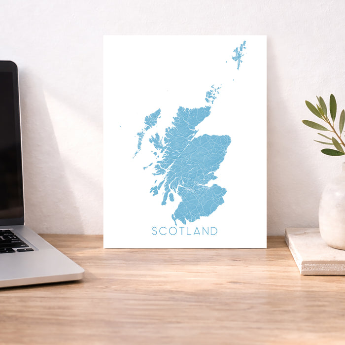 Map of Scotland on a white background next to a laptop on a wooden desk.