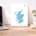 Map of Scotland on a white background next to a laptop on a wooden desk.
