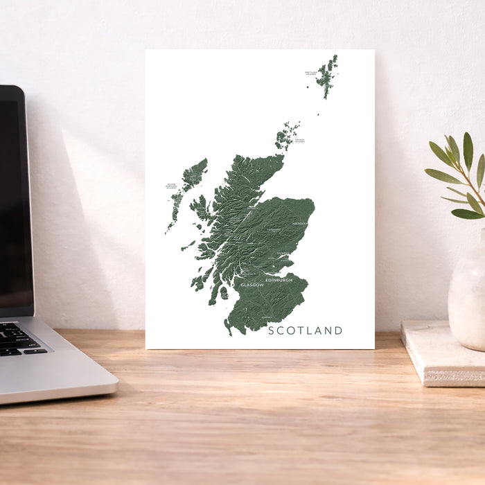 Map of Scotland on a white background next to a laptop on a wooden desk.