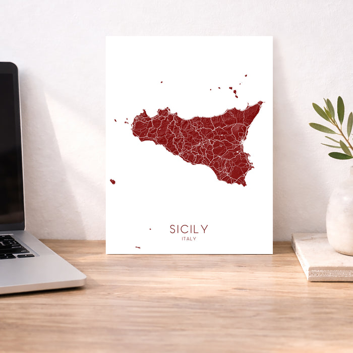 Map of Sicily on a white background next to a laptop on a wooden desk.