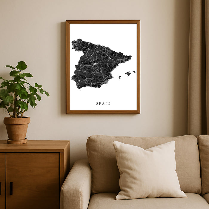 Framed map of Spain on a wall above a sofa with a plant beside it.