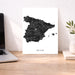 Map of Spain on a white background next to a laptop on a wooden desk.