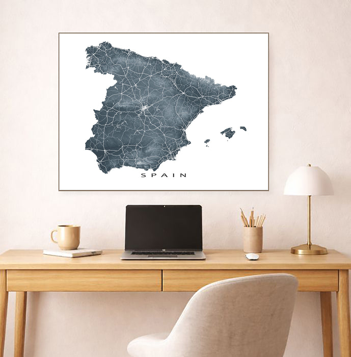 Map of Spain on a wall above a desk with a laptop and lamp.