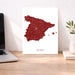 Map of Spain on a white background next to a laptop on a wooden desk.