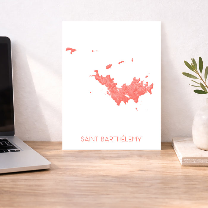Map of Saint Barthélemy on a white background displayed on a desk with a laptop and plant.