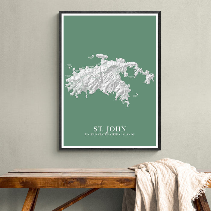 Framed map of St. John, U.S. Virgin Islands on a green background, hanging above a wooden bench.