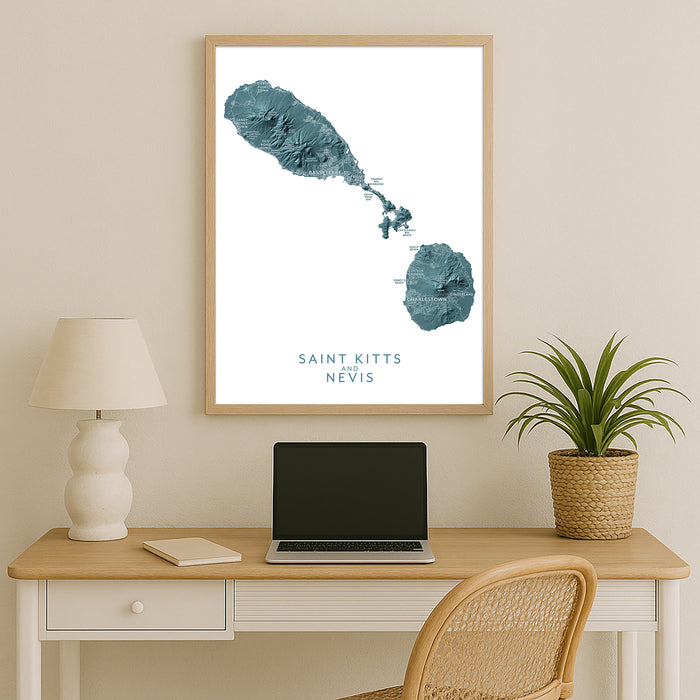 Framed map of Saint Kitts and Nevis above a desk with a laptop and lamp.