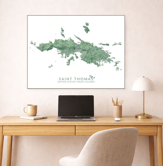 Framed map of Saint Thomas on a wall above a desk with a laptop and lamp.
