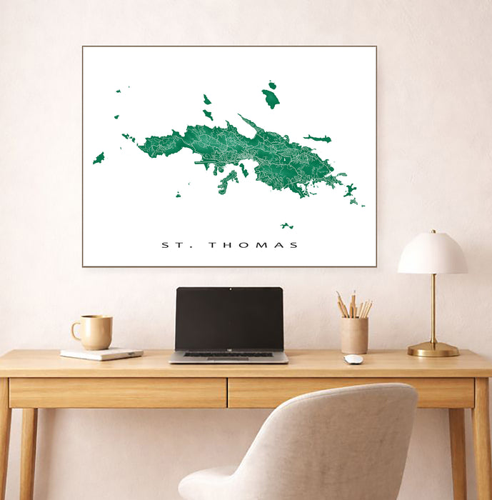 Framed map of St. Thomas on a wall above a desk with a laptop and lamp.