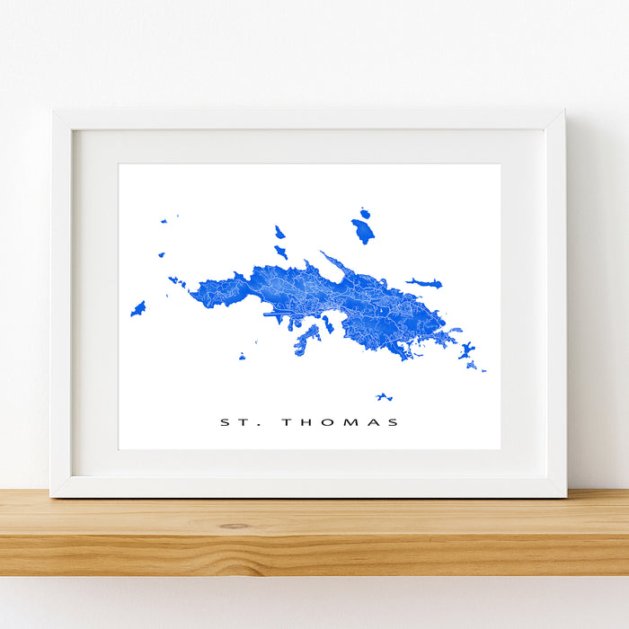 Framed map of St. Thomas on a white wall with a wooden shelf.