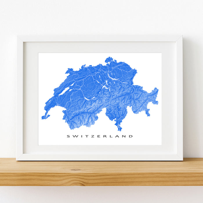 Framed map of Switzerland with a white border on a wooden shelf.
