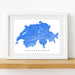 Framed map of Switzerland with a white border on a wooden shelf.