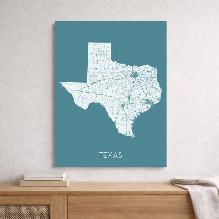 Map of Texas on a teal background hanging on a wall above a wooden surface.