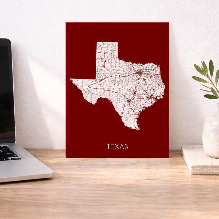 Map of Texas on a red background on a desk with a laptop and plant.