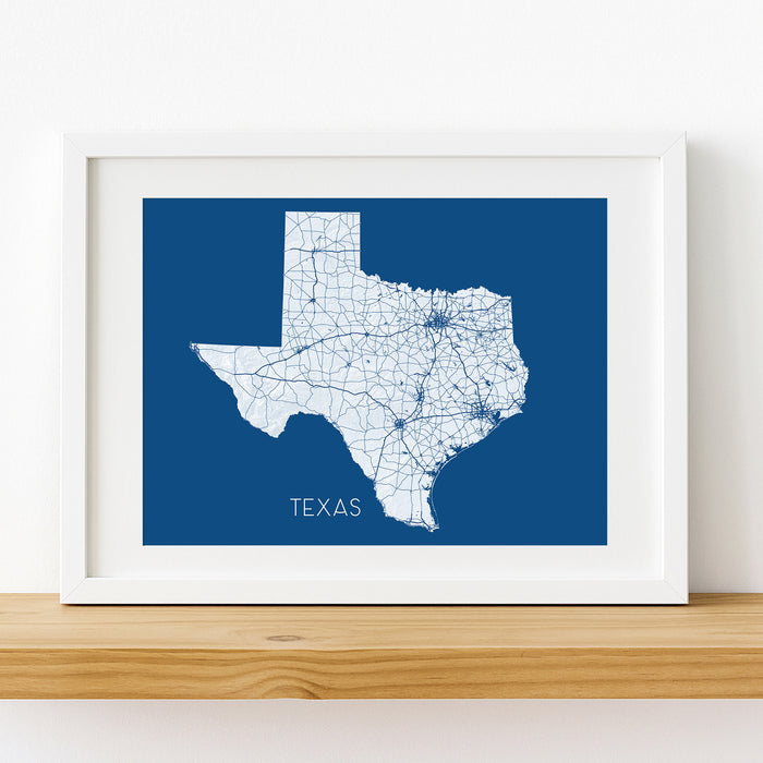 Framed map of Texas on a blue background with white roads, set against a white wall.