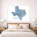 A large framed Texas state map print in shades of blue and white hangs above a wooden bed in a bright, modern bedroom with matching bedside tables and lamps.