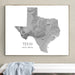 A framed gray topographic map print of Texas with the text 'TEXAS ROAD TRIP - SPRING 2026' below the map, displayed on a beige wall above a white bench with a light blue draped cloth.