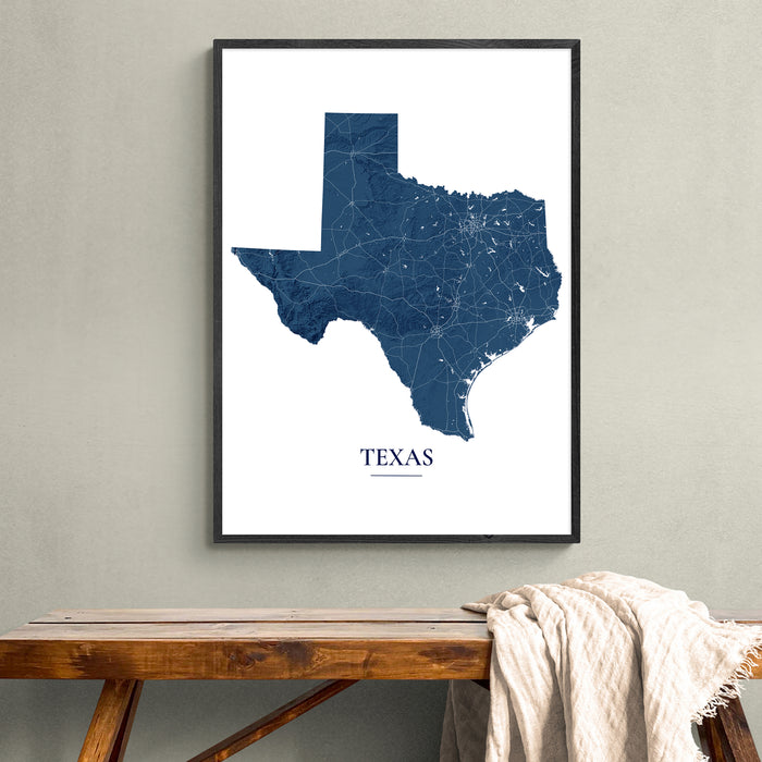 A framed Texas state map art print in navy blue and white, hanging on a light gray wall above a rustic wooden bench with a draped cream throw blanket.