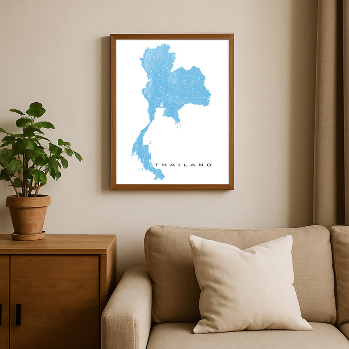 Framed map of Thailand on a wall above a beige sofa with a plant beside it.